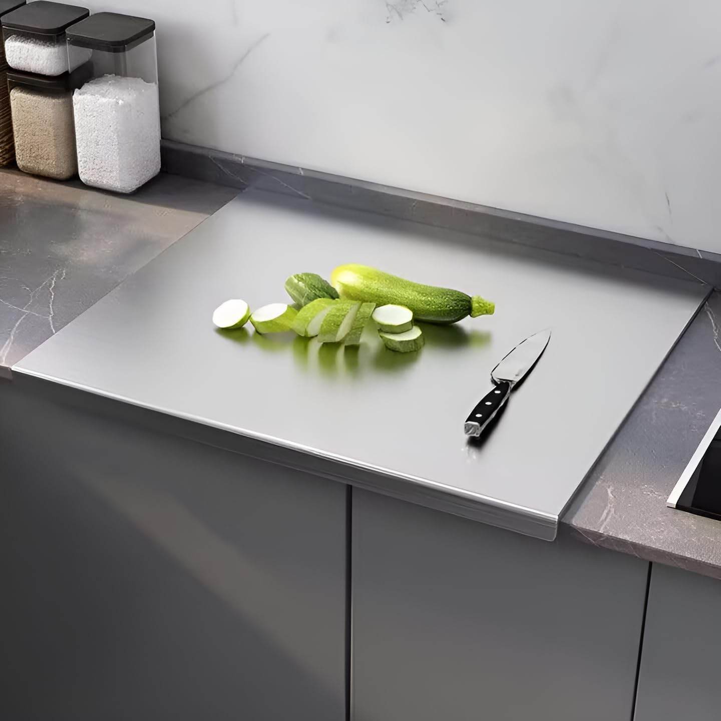 Glass cutting board with sliced zucchinis and a knife on a kitchen counter.