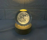 Glowing moon lamp in a clear spherical glass on wooden base with power cord, dark background