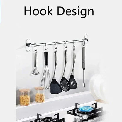 Stainless steel kitchen utensils hanging on wall-mounted hook rack above gas stove with blue flame