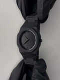 Matte black minimalist wristwatch with black dial and Roman numerals held by gloved hands