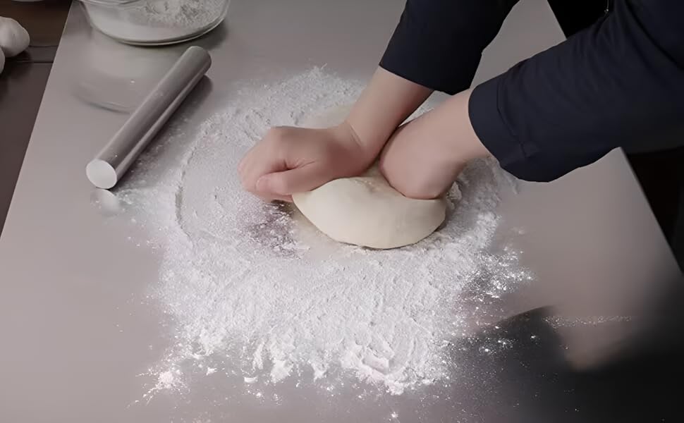 Person kneading dough on a floured surface with a rolling pin nearby.