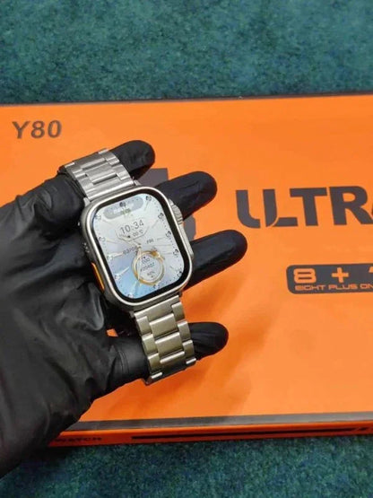 Hand wearing black glove holding Y80 Ultra 8-in-1 smartwatch with silver metal band over orange box